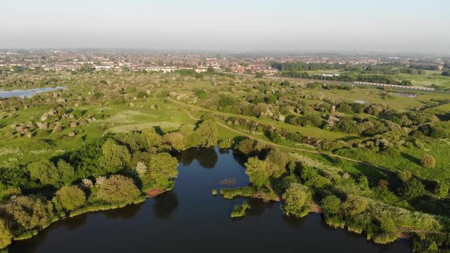 Flying over the Bardag Lake in the Eastbrookend Country Park at sunset and two trains passing by into the distance.