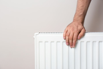 Man warming hand on heating radiator against color background. Space for text