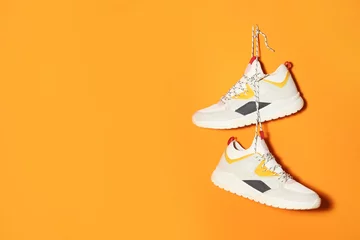 Foto op Plexiglas Pair of stylish sneakers hanging on color wall, space for text © New Africa