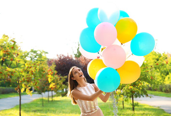 Beautiful teenage girl holding colorful balloons in park