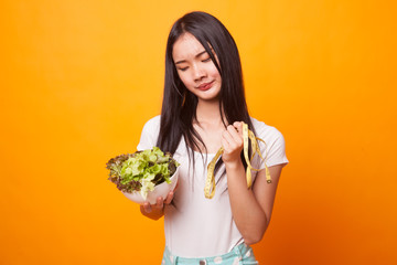 Unhappy Asian woman with measuring tape and salad.