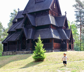 Little two years old boy running and playing in front of the Gol Church,  a stave church originally built in Gol city, but now located in the Norwegian Museum of Cultural History at Bygdy in Oslo. © nachosuko