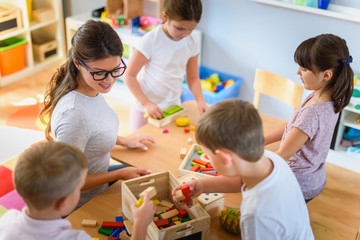 Preschool teacher with children playing with colorful wooden didactic toys at kindergarten - obrazy, fototapety, plakaty