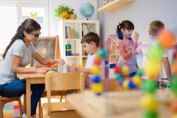 Preschool teacher with children playing with colorful wooden didactic toys at kindergarten - obrazy, fototapety, plakaty