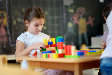 Cute girl plays with toy building blocks at kindergarten