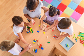 Preschool teacher with children playing with colorful wooden didactic toys at kindergarten. View from above.