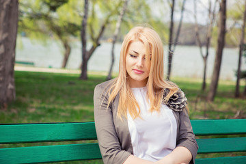 woman looking down sadly thinking sitting on a bench in a green park