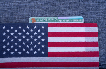 Green Permanent resident card covered American (USA) flag on blue fabric surface.