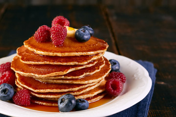 Stack of pancakes with berries and maple syrup on dish