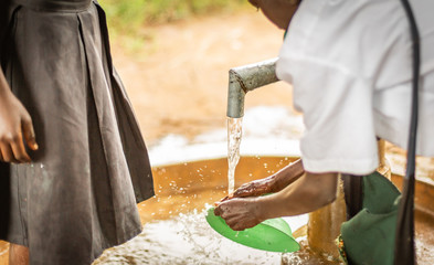 African boy cleans his plastic dish at the local town water pump.