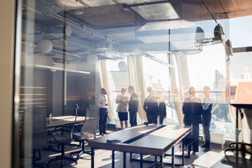 Wide angle view of group of successful businespeople discussing projects behind glass wall in office, copy space