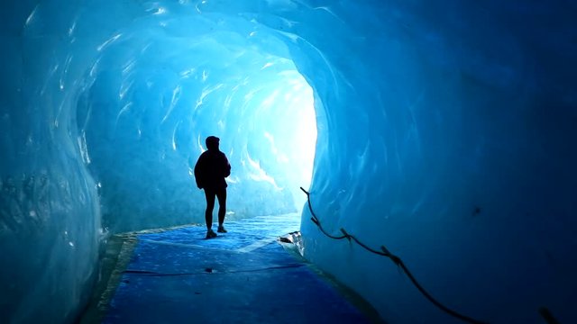 A girl is walking under the ice. A huge tunnel has been built inside the ice, so people can walk inside and enjoy the view.