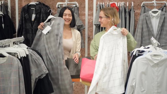 Stylist selects a set of casual clothes to women in a store at shopping mall.