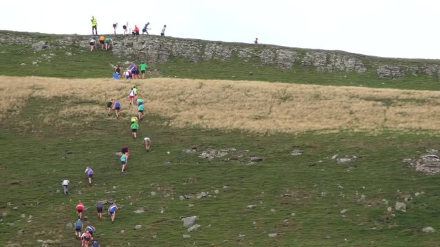 Fell race at the muker show 2018 showing runners reaching the top of a very steep hill.