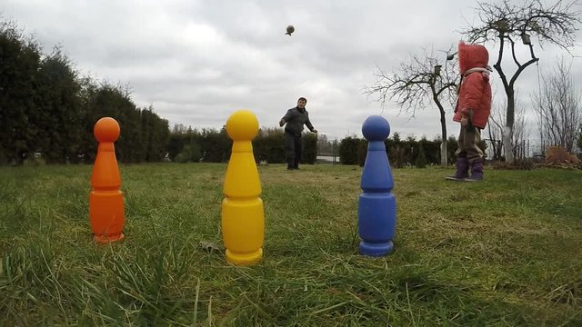 The father teaches a young daughter to throw howler blaster rocket and hit the bowling pin targets. Slow motion