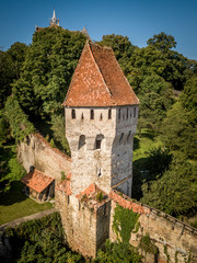 Aerial view of rustic medieval defensive tower with orange, red roof, loopholes on the city walls of Sighisoara with blue sky