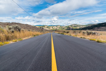 Naklejka premium Rural highway disappearing into distance surrounded by grasslands in autumn