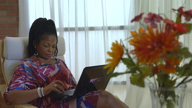 Flowers in the foreground with a lovely African American woman using a laptop scrolling through a website while doing some online shopping.