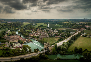 Aerial panorama of famous Italian medieval fortified bridge and village with cloudy sky and blue waterway in Valeggio sul Mincio Italy