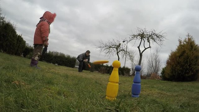 Father throws flying spin disc and hits yellow bowling pin target. Slow motion