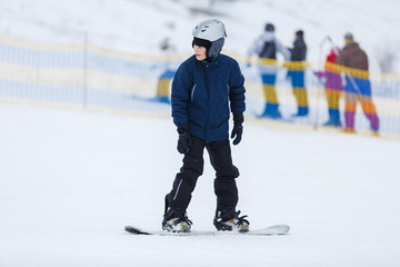 cute young boy, brave kid in gray helmet and orange googles, in blue jacket snowboarding on white snow mountain. winter sport, active lifestyle concept