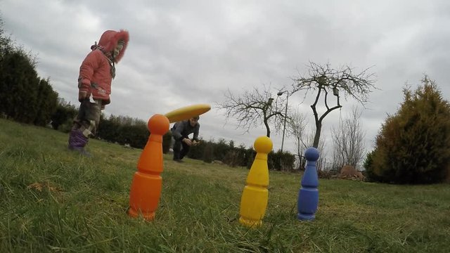 Father throws flying spin disc and hits orange bowling pin target. Slow motion