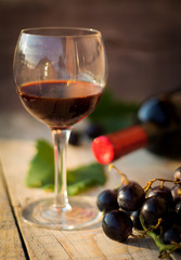 Wine glass with black wine. Bottle of wine and grapes in the background