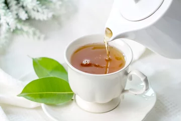 Crédence de cuisine en verre imprimé Theé Gros plan versant du thé noir chaud dans une tasse de thé blanc, concept de l& 39 heure de la cérémonie du thé