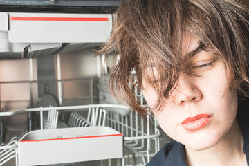 Tired beautiful girl near the dishwasher in the kitchen