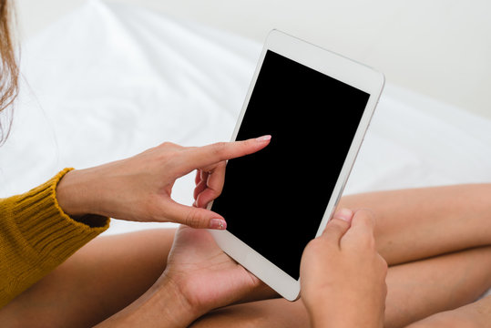Young Asian women using tablet mock up blank black screen in her bedroom alone by swiping it with her finger in the warm light sunshine day. LGBT women swipe on tablet in the bedroom.