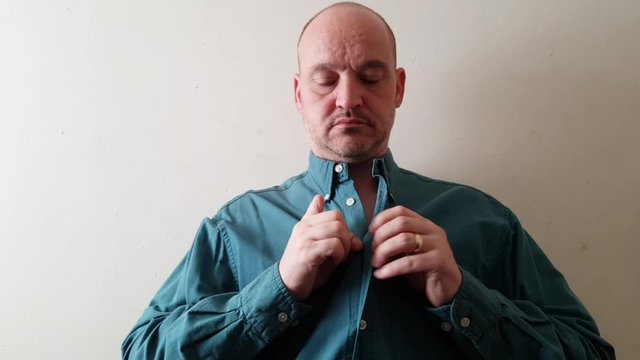 Male with a partially amputated index finger on his right hand buttoning up a green shirt.