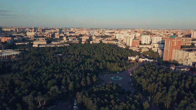 Aerial drone flight over the huge park with mixed forest in the center of Chelyabinsk city, sunny evening in the capital of South Ural, Russia