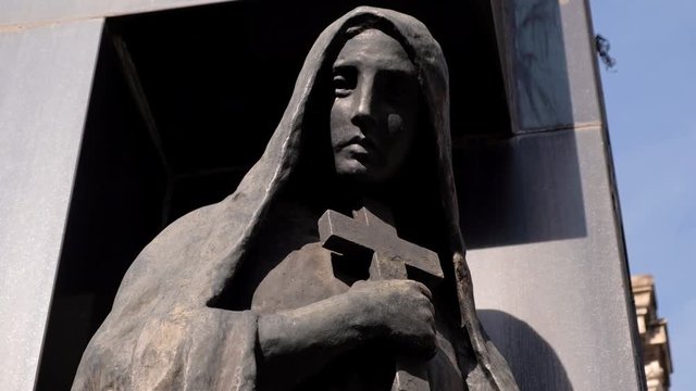 Woman holding cross made of black stone statue in La Recoleta Cementery at daytime tight shot