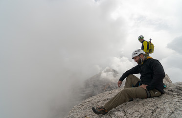 young male mountain climber on a Dolomite mountain peak enjoying the view from the summit and his mountain guide standing behind him