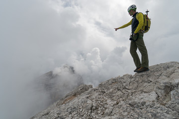 young male mountain guide on a Dolomite mountain peak pointing to the landscape and explaining the view