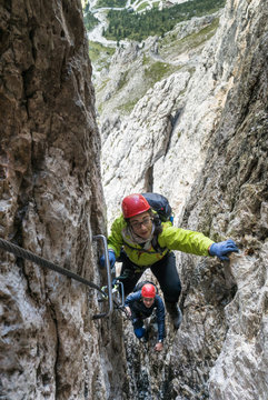two young female montain climbers climb through a narrow crack on a steep climb in the Dolomites of Alta Badia in northern Italy