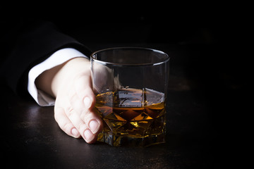 Whiskey glass in hand on the dark bar counter, selective focus