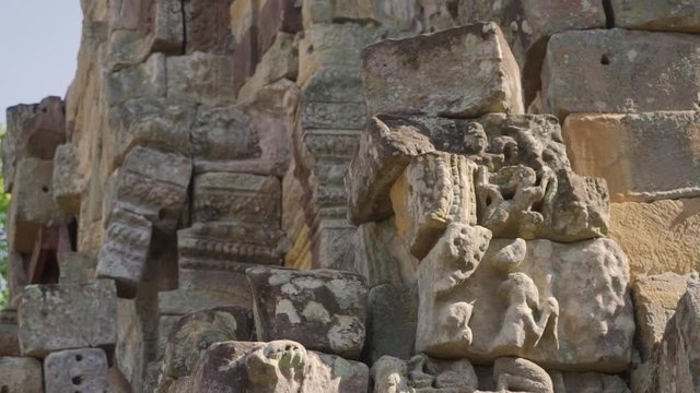 Slow pan up a pile of rubble from an ancient Khmer temple; ancient stonework; ancient carving.