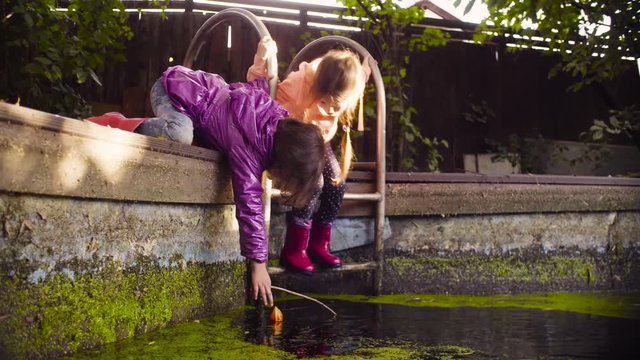 Crane shot. Two girls playing near the old pool overgrown with duckweed. A girl catching orange flower