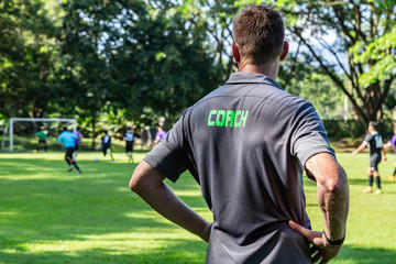 Male football or soccer coach watching his team play at a beautiful soccer field