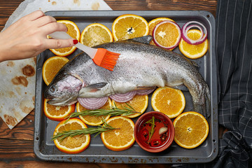 Fresh salmon lying on a baking sheet with oranges. Hand chef with a brush smears salmon oil. The concept of cooking salmon.