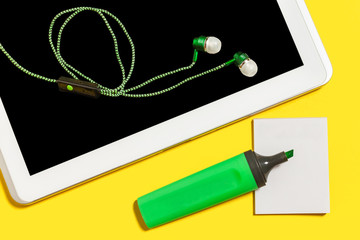 collection of business or education accessories. green pencils, headphones, paper stickers, opened marker and tablet pc lying on a yellow background. concept of the office gadgets and stationary