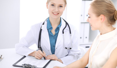 Blonde female doctor and patient talking in hospital office. Health care and client service in medicine