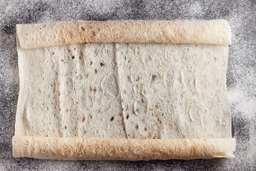 Rolls of fresh flatbread on black baking surface, top view. Traditional bread in Middle East and Central Asia. It can be used for wraps, rollups, crackers and pizza.