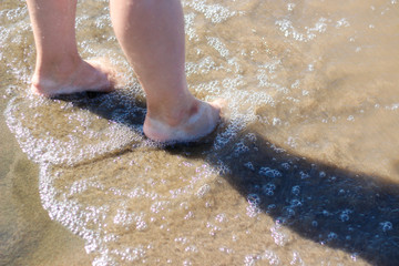 Girl's feet on the beach. Sea waves and legs