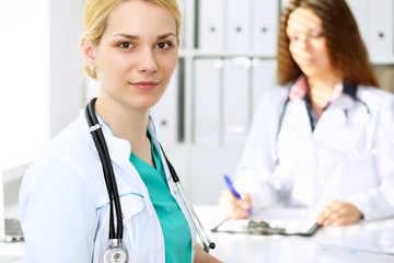 Doctor woman or nurse standing in a hospital office with her colleague in the background. Healthcare and medicine concept