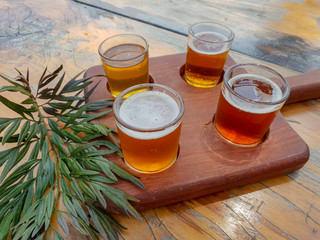 Four beer glasses on wooden board on outdoor table.