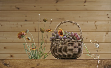 Juicy grapes in a basket and flowers in a vase on a wooden wall background