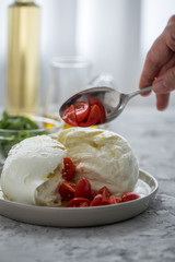 Frau bereitet Büffelmozzarella zu Tomate Mozzarella Salat mit Basilikum, Olivenöl und weißen Balsamico zu