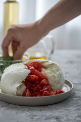 Frau bereitet Büffelmozzarella zu Tomate Mozzarella Salat mit Basilikum, Olivenöl und weißen...
